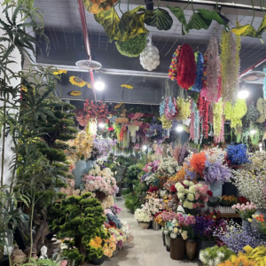 Wide view of PJTL artificial flower wholesale showroom aisle with hanging garlands and bulk floral displays, Shantou China