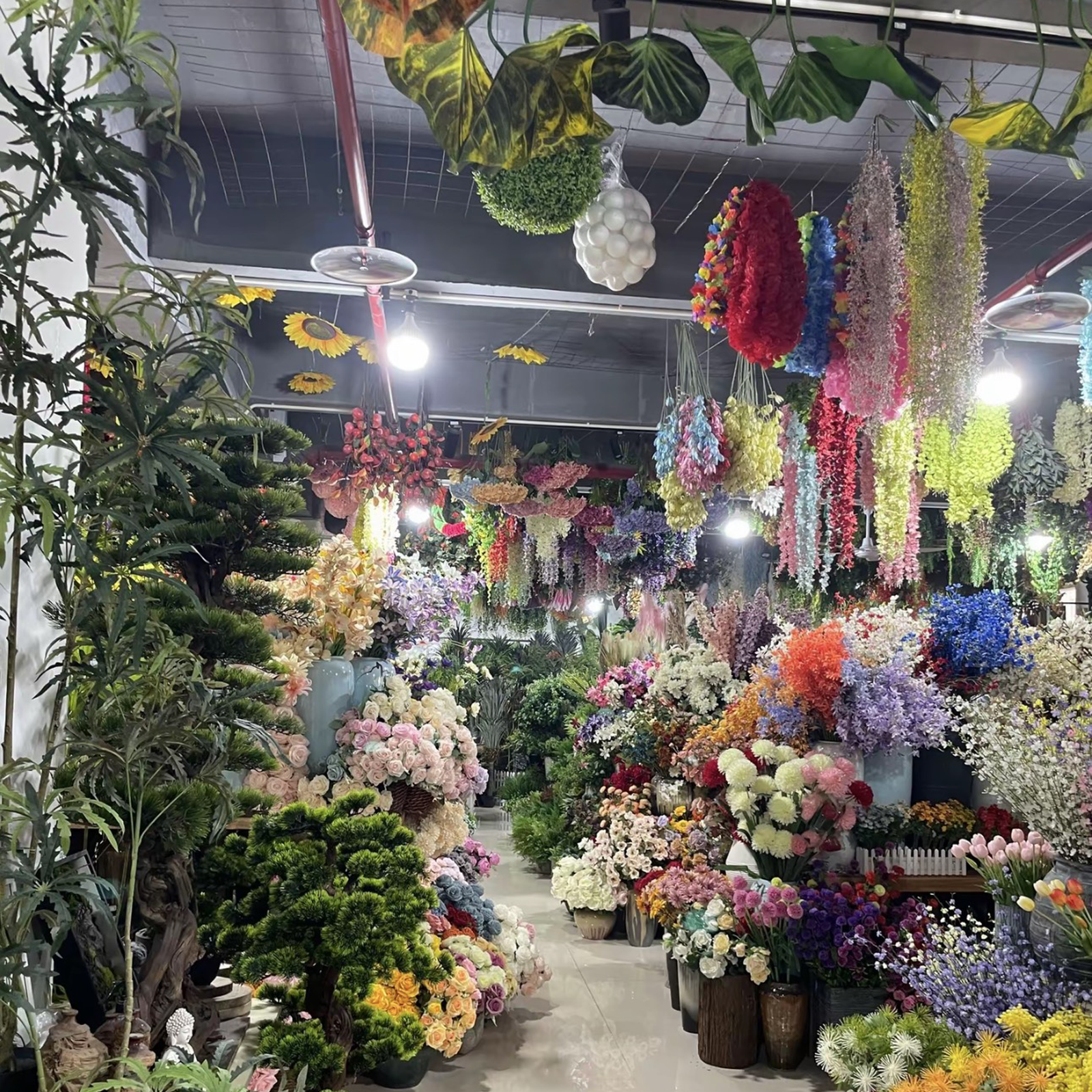 Wide view of PJTL artificial flower wholesale showroom aisle with hanging garlands and bulk floral displays, Shantou China
