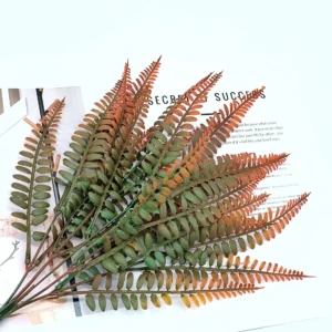 Rust orange and olive green artificial autumn fern leaf bushes in a styled flat-lay display