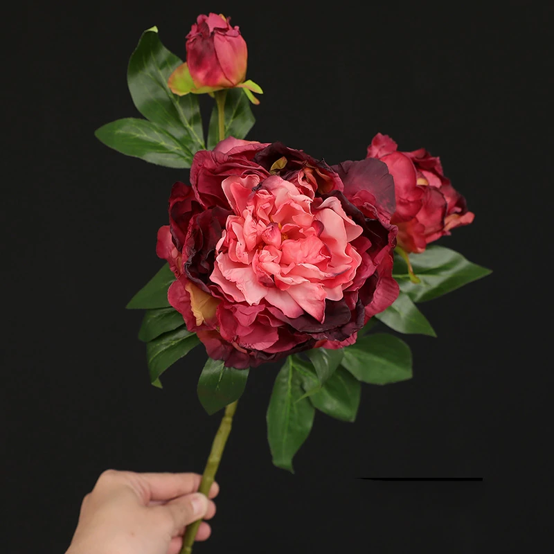 Handheld view of burgundy artificial three-head peony spray