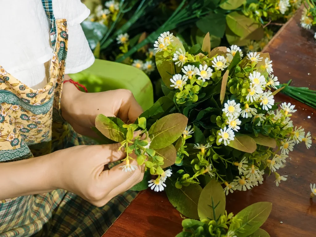 A worker holding artificial flower branches with white blooms and green leaves.