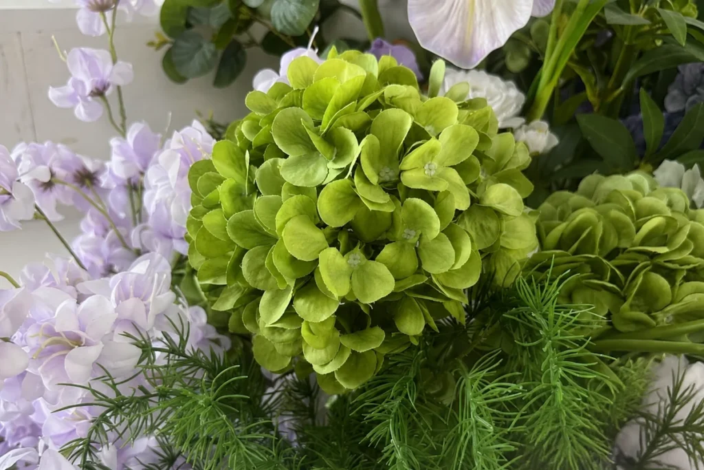 Close-up of a green artificial hydrangea with clustered petals and surrounding foliage.