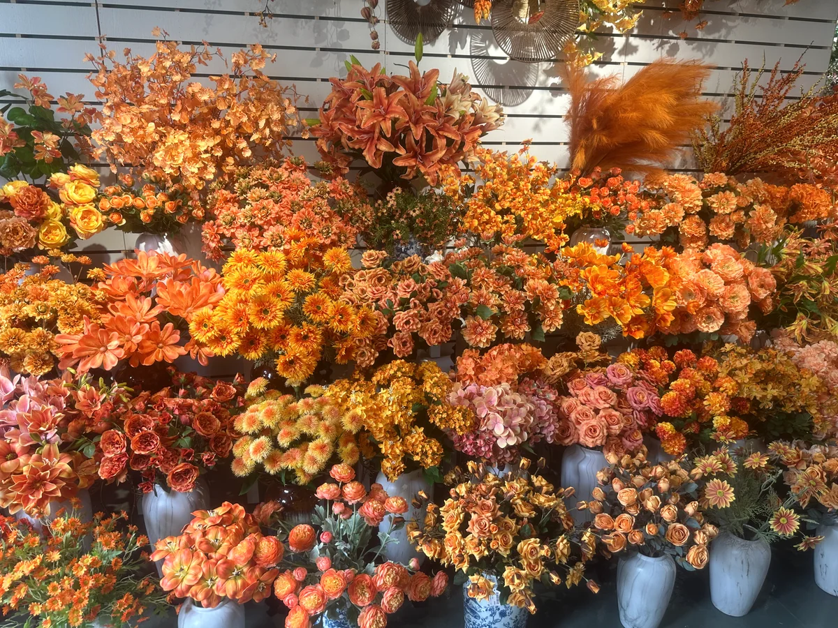 Orange and peach artificial flowers, including roses and lilies, displayed in showroom vases.