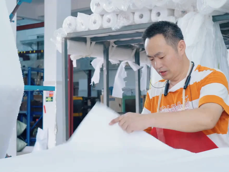 A worker spreading white sheet material at a worktable in the flower production workshop.