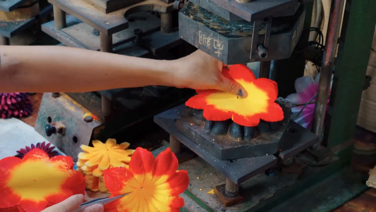 Hands positioning an orange and yellow artificial flower petal piece on a metal mold.