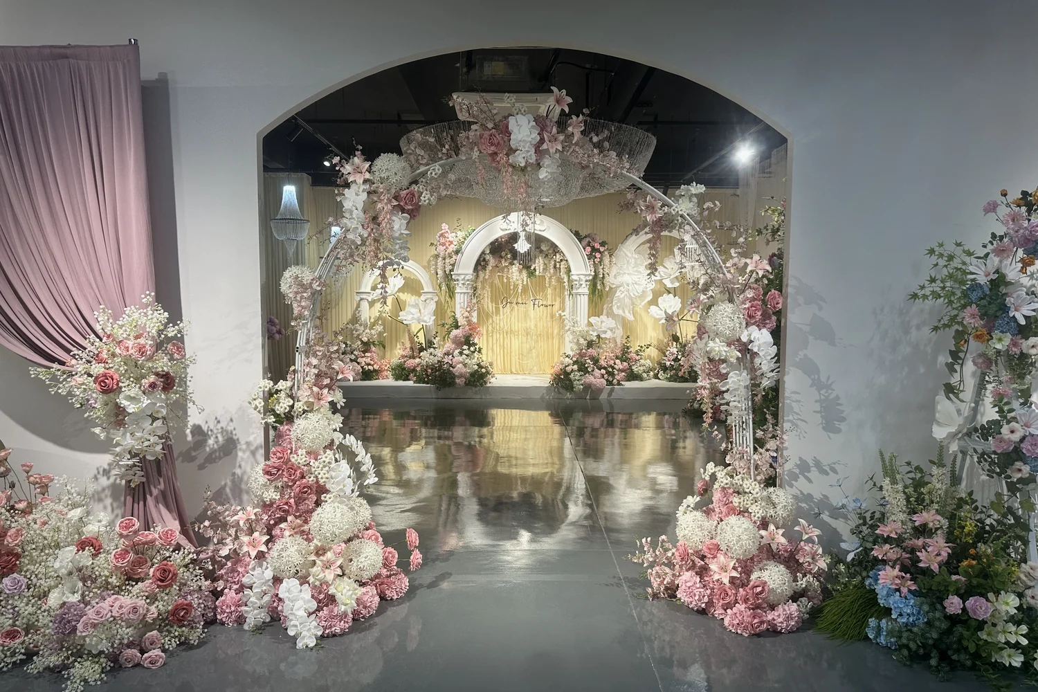 Pink and white artificial flowers arranged around an archway in a showroom.