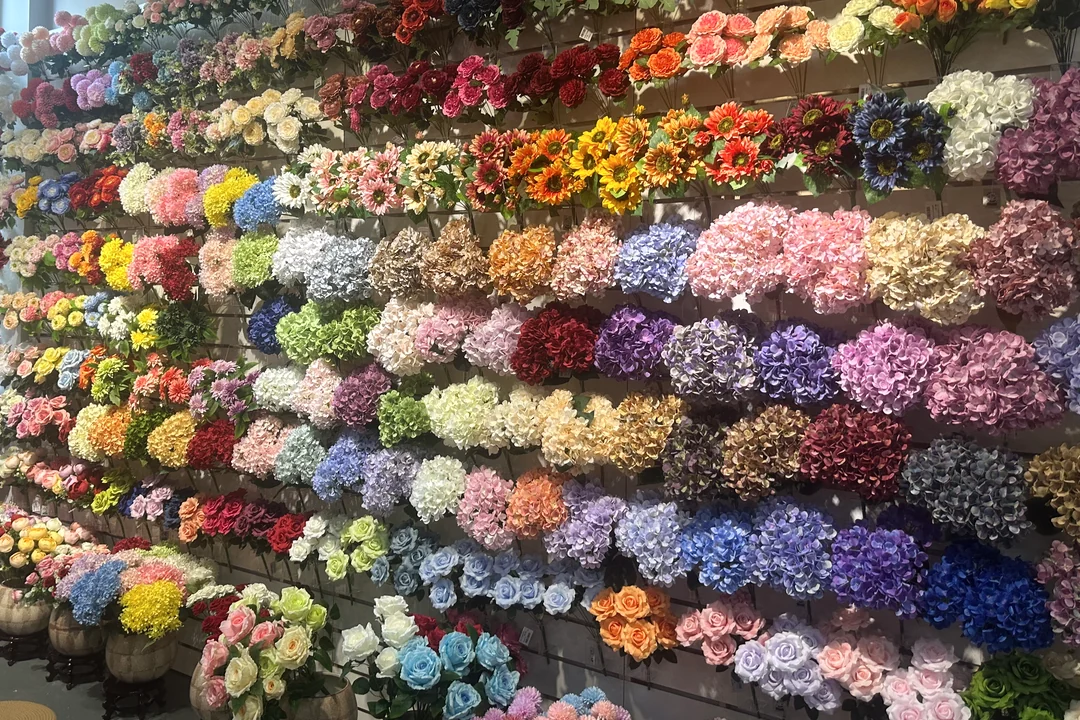 Rows of artificial roses, hydrangeas and other flowers in multiple colors on a showroom display wall.