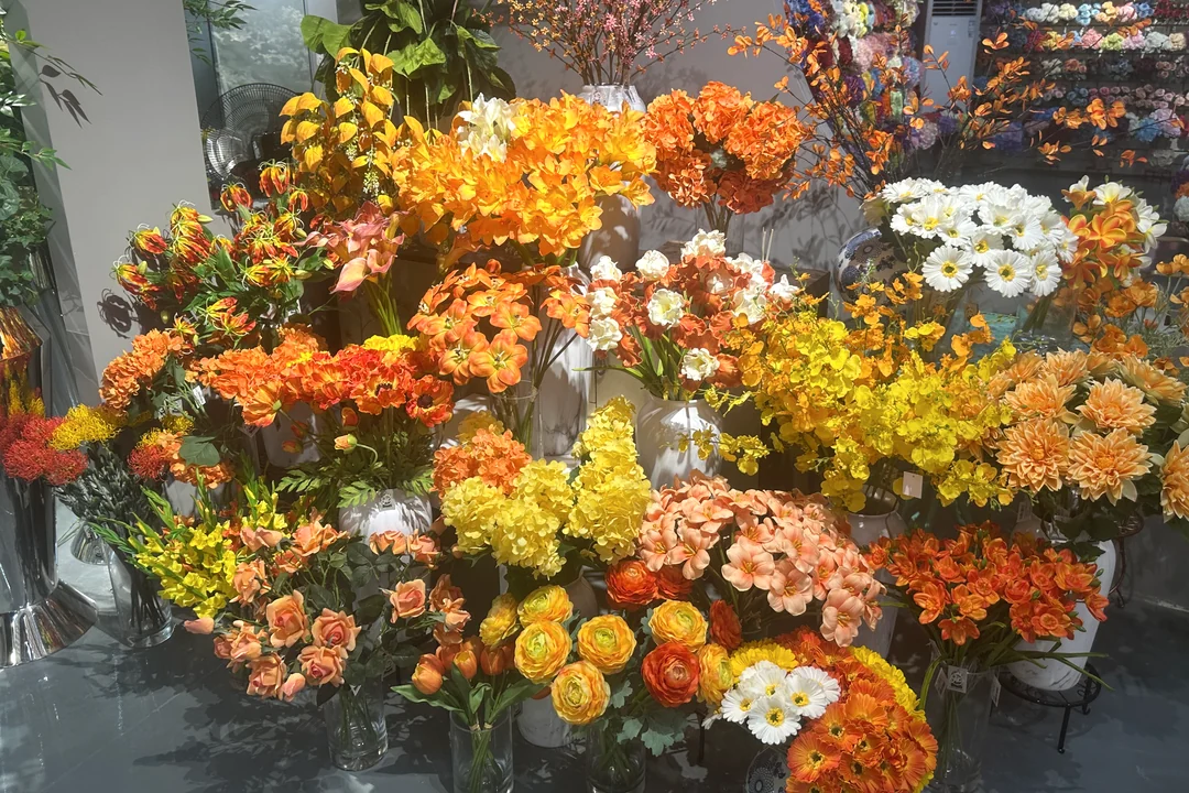 Orange, yellow and white artificial flower arrangements displayed in vases in a showroom.