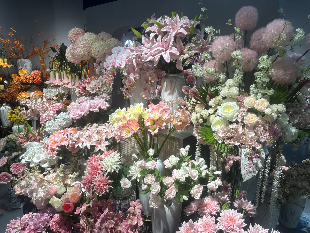 Pink and white artificial lilies, orchids, roses and other flowers arranged in showroom vases.