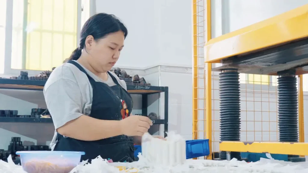 A worker handling white flower petal cutouts beside a production machine.